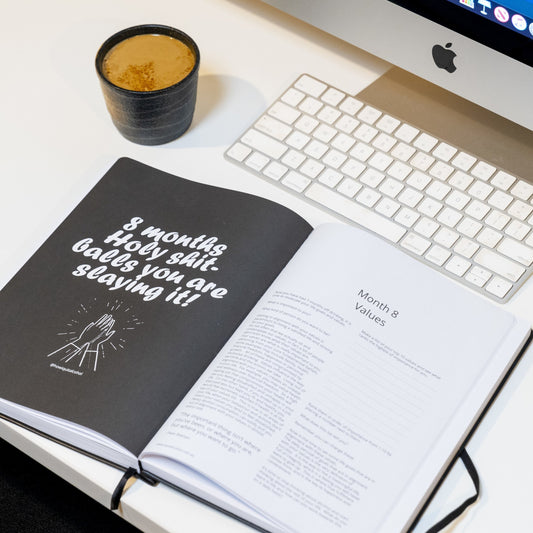 the How I quit Alcohol Playbook journal open to a page, resting near a computer with a coffee.